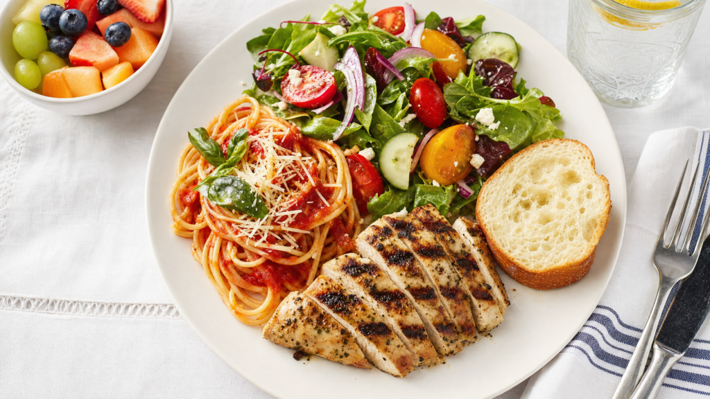Pasto completo equilibrato con pasta, proteine, verdure e frutta visto dall'alto